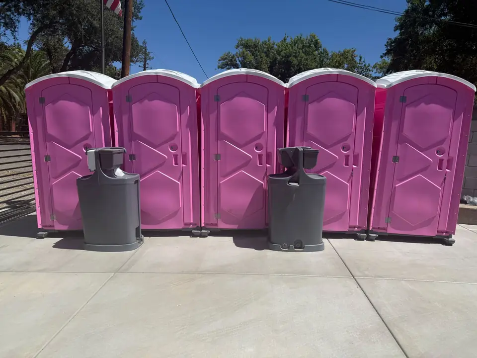 Five pink porta potties with two hand-wash stations at an event