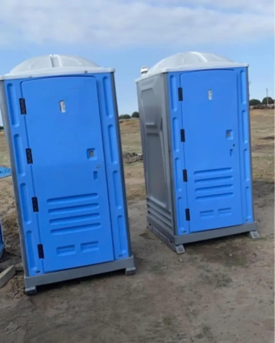 Two blue standard porta potties on a dirt job site