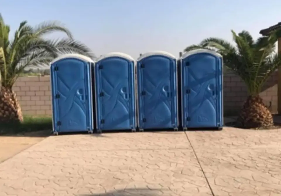 Four blue standard porta potties lined up on a concrete pad