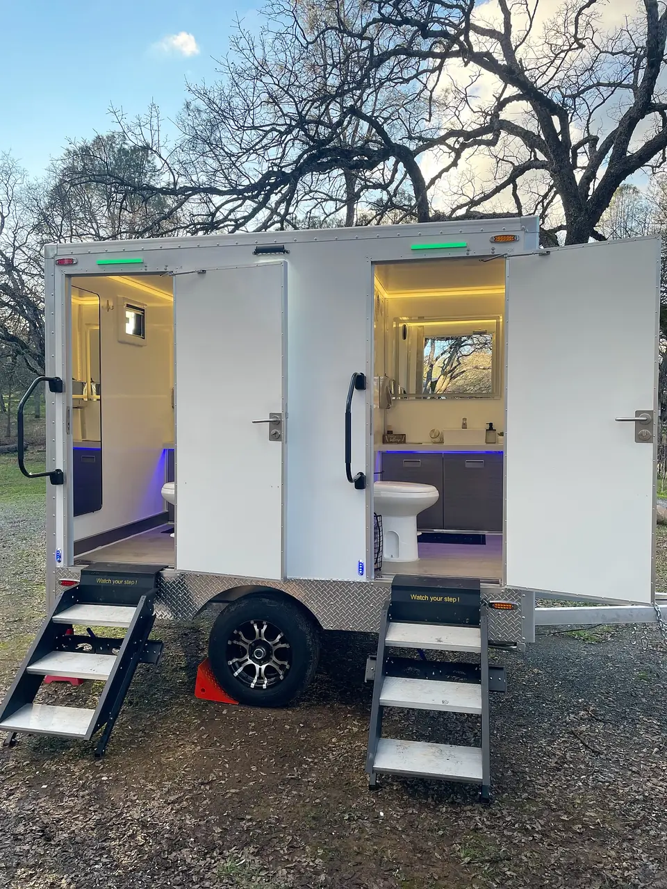 Two-stall restroom trailer with both doors open and lights on
